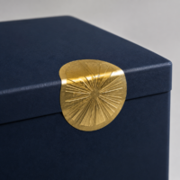 Close-up of a round gold foil seal sticker label on a matte navy gift box